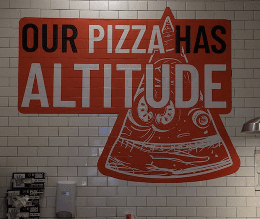 Wall art showing a pizza slice with the slogan about pizza's altitude.